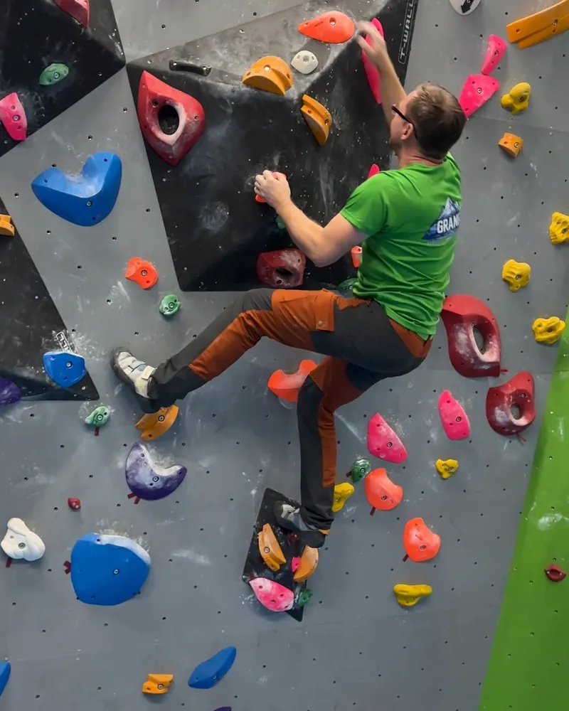 Wspinacz w szerokim kroku pokonuje trasę na ściance boulderowej w Jumpout