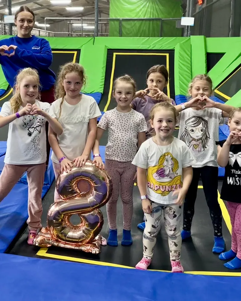 Solenizantka z gośćmi i animatorką pozuje na trampolinach z balonem w kształcie ósemki